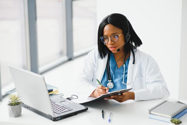 Il medico africano indossa l'auricolare consulta il paziente e effettua la videochiamata online con la webcam sullo schermo del laptop.
