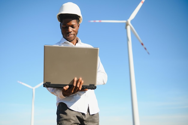 African Engineer standing and hoding laptop with wind turbine