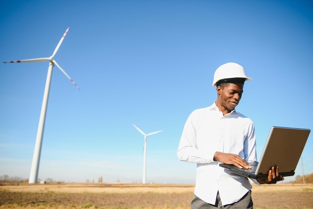 African Engineer standing and hoding laptop with wind turbine