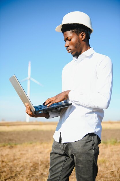 African Engineer standing and hoding laptop with wind turbine