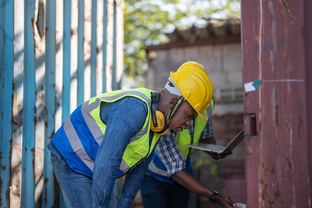 African Engineer Technician holding laptop for checking and inspecting on site containers area