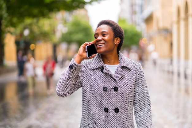 African ethnicity business woman in the city portrait of finance woman walking down the street talking on the phone smiling