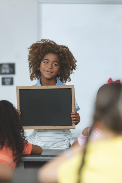 African ethnicity schoolboy holding a slate and looking at camera in classroom