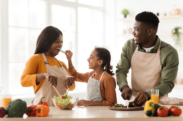 Famiglia africana che si alimenta a vicenda divertendosi a preparare l'insalata al coperto