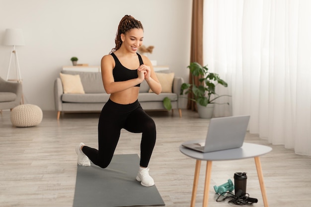 African female doing forward lunge watching video on laptop indoors