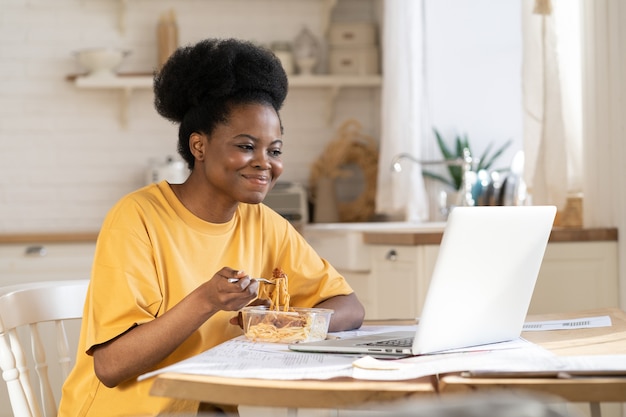 Le donne africane mangiano e guardano video o webinar sul laptop o fanno teleconferenze con gli amici in pausa