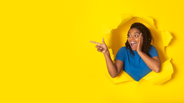 African female pointing finger aside posing in torn yellow paper