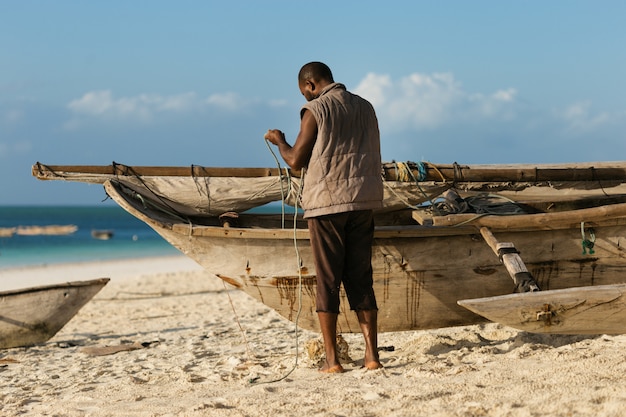 Foto pescatore africano che ripara la sua vecchia barca di legno