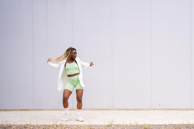 African fit woman dancing in front of an urban wall with sportive clothes and braided hair