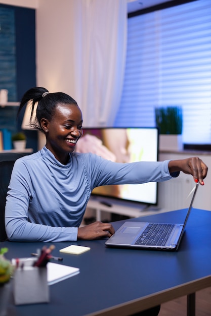 African freelancer working remote on deadline sitting on desk in home office in the evening. Black entrepreneur sitting in personal workplace writing on keyboard.