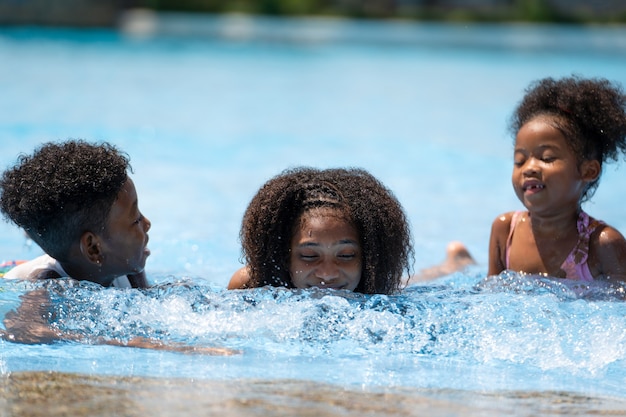 アフリカの女の子と男の子が遊園地のプールに座って水遊び。コンセプトキッドは純粋な喜びと興奮を表現しています