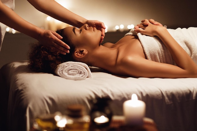 African girl having face massage, relaxing in spa salon, side view