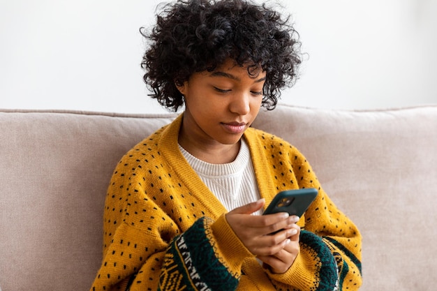 Африканская девушка держит смартфон с сенсорным экраном, печатая страницу прокрутки дома