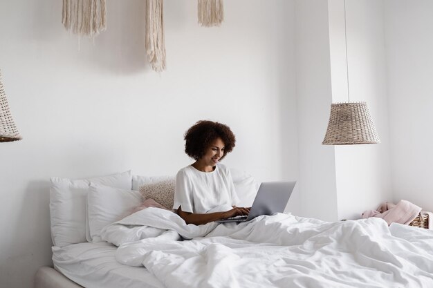 African girl manager with laptop have online video meeting with colleagues and business partners in cozy bed at home in the morning Team discussion trends and tasks