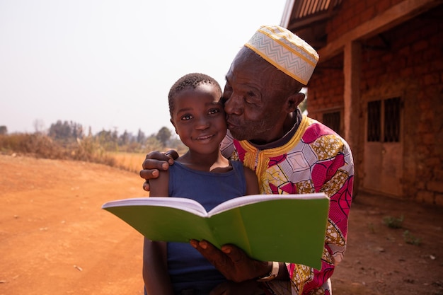 African grandfather kisses his grandson as they read a book together Love between grandfather and grandson