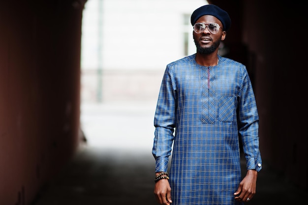 African guy in blue authentic costume, eyeglasses and beret. Fashionable nigerian man.