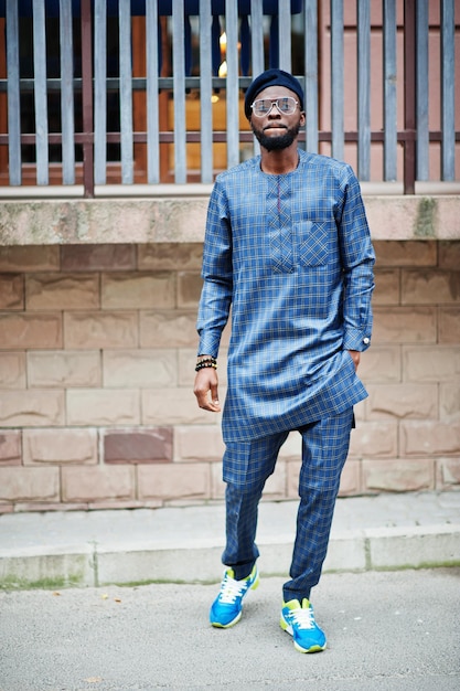 African guy in blue authentic costume, eyeglasses and beret. Fashionable nigerian man.