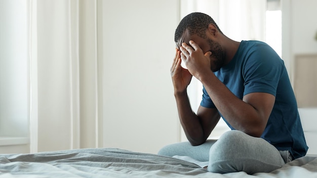 African Guy Crying Covering Face With Hands Sitting In Bedroom