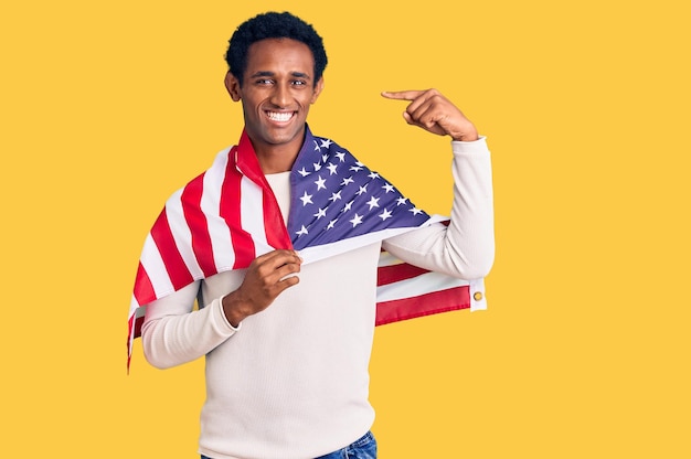 African handsome man holding united states flag pointing finger to one self smiling happy and proud