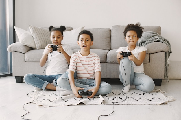 Photo african kids playing video games. children in light clothes. controller in hands of children.