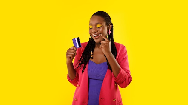 African lady holding credit card dreaming about shopping yellow background