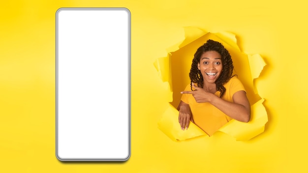 African Lady Pointing At Cellphone Screen On Torn Yellow Background