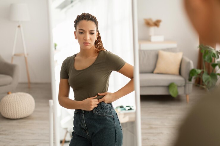 Photo african lady touching belly after weight gain near mirror indoor