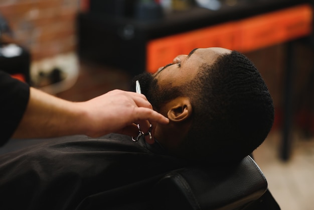 Африканский клиент-мужчина стригется в парикмахерской от профессионального парикмахера