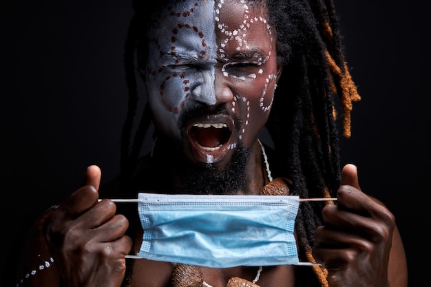 African male scream by pain, he is going to wear medical mask on face, stand with opened mouth. isolated black wall