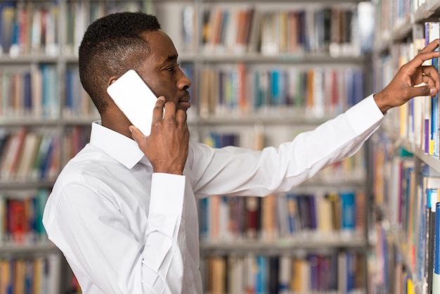 African Male Student Talking On The Phone In Library  Shallow Depth Of Field