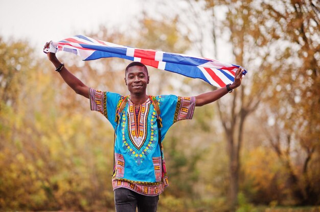 African man in africa traditional shirt on autumn park with Great Britain flag.