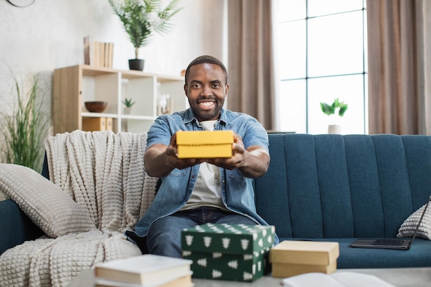 African man in denim shirt holding gift box on couch