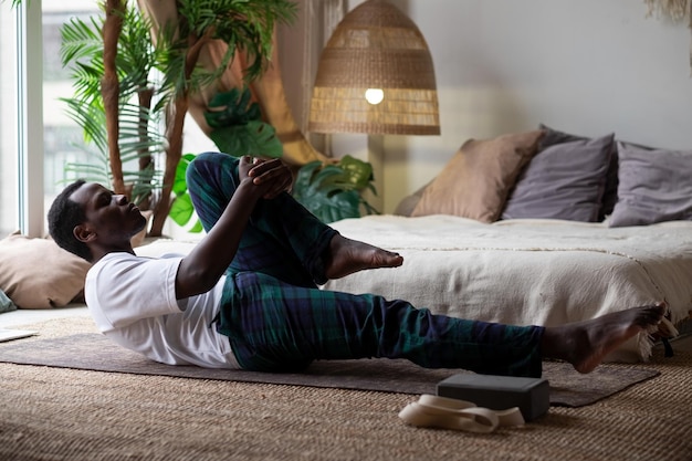 African man doing yoga on the floor practicing the Supported One Legged Wind Relieving Pose