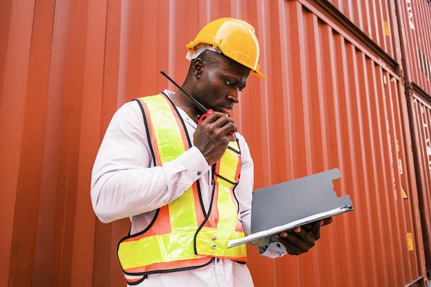 Photo african man engineer worker in yellow hard hat high visibility vest talking on walkietalkie radio