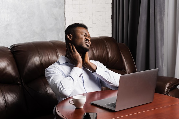 아프리카 남자는 사무실에서 온라인으로 노트북을 가지고 장시간 일한 후 목 통증을 느낀다