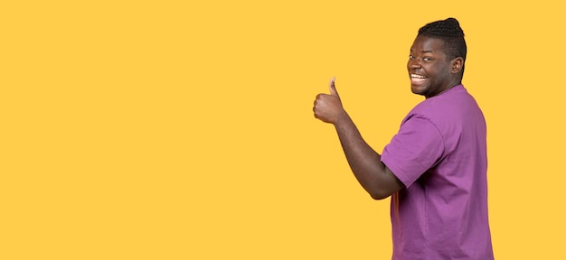 African man gesturing thumbs up at camera over yellow background