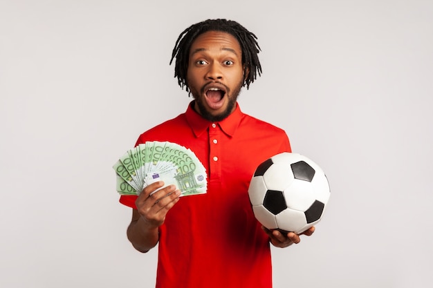 African man holding euro banknotes and soccer ball, betting on\
sport, victory.