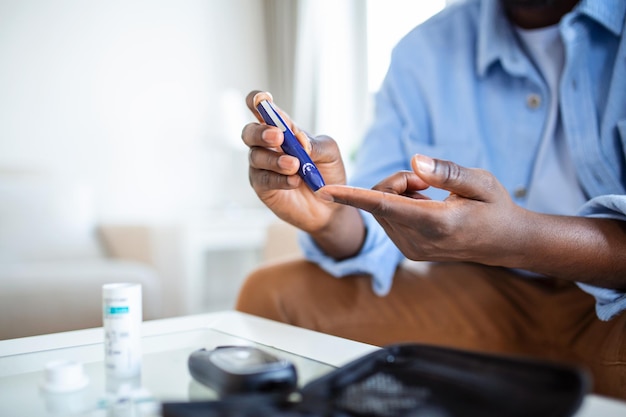 Африканский мужчина сидит дома на диване и берет кровь из пальца из-за диабета