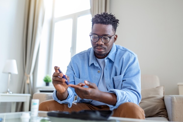 African man is sitting at the sofa and taking blood from his finger due to diabetes The daily life of a man of AfricanAmerican ethnicity person with a chronic illness who is using glucose tester