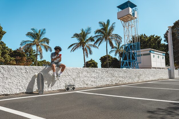 African man listening music with vintage boombox stereo outdoor while using mobile phone - Focus on face