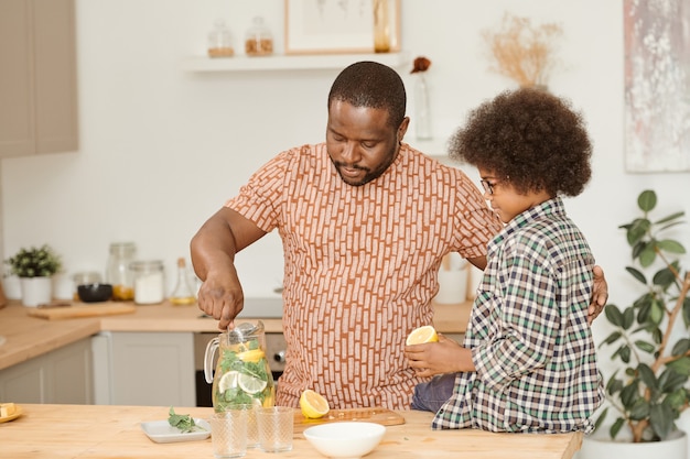 African man mixing lemonade in jug while his little son looking at him