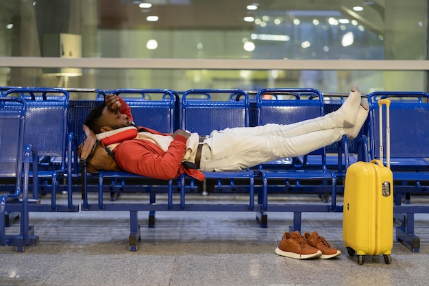 비행기를 기다리는 동안 낮잠을 자는 아프리카 남자 공항 수하물 근처 벤치에 누워 있는 흑인 남자