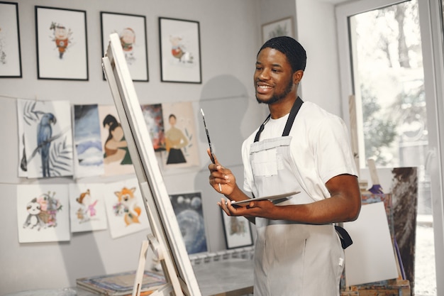 L'uomo africano nella classe di pittura disegno su un cavalletto.