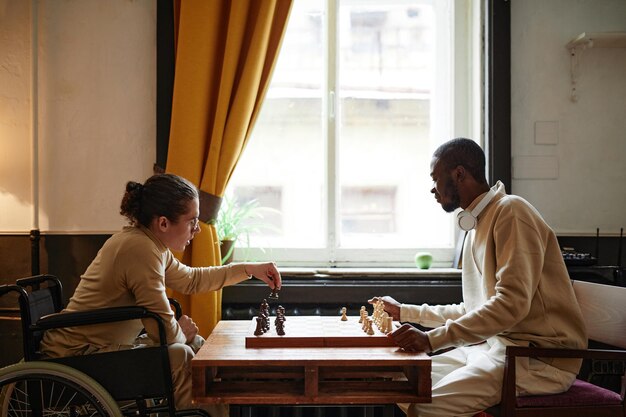 African man playing chess together with his friend with disability they sitting in the room