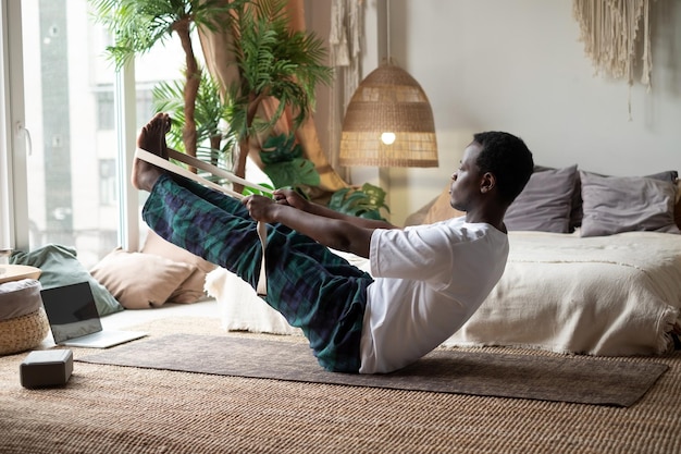 African man practicing yoga indoors doing Boat Pose or Paripurna Navasana during online class