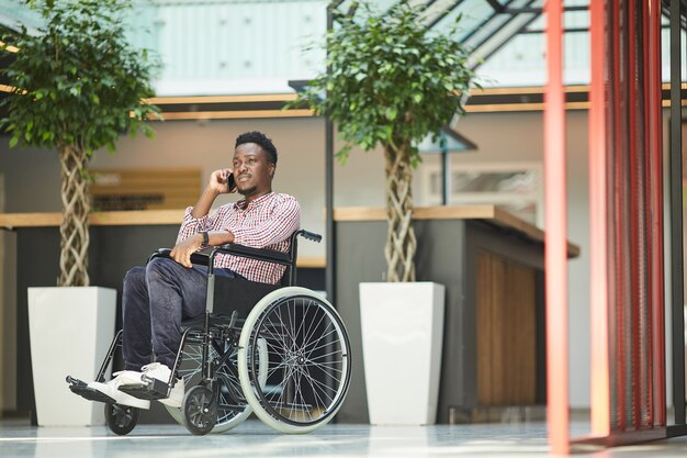 African man sitting in wheelchair he has conversation on mobile phone at office building