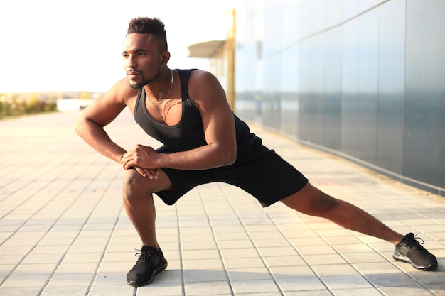 African man in sports clothing warming up outdoors, at sunset or sunrise.