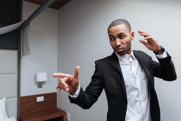 African man in suit posing in hotel room, pointing and looking away