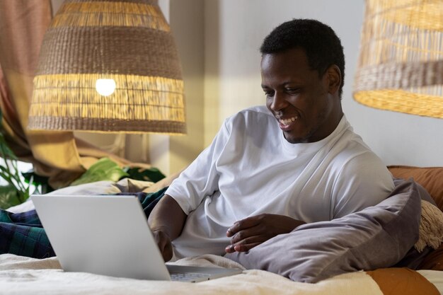 African man surfing the internet in his bed Working from home in quarantine lockdown Social distancing concept