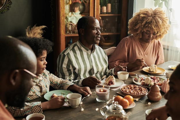 African man talking at table while eating dessert together with\
his family at home